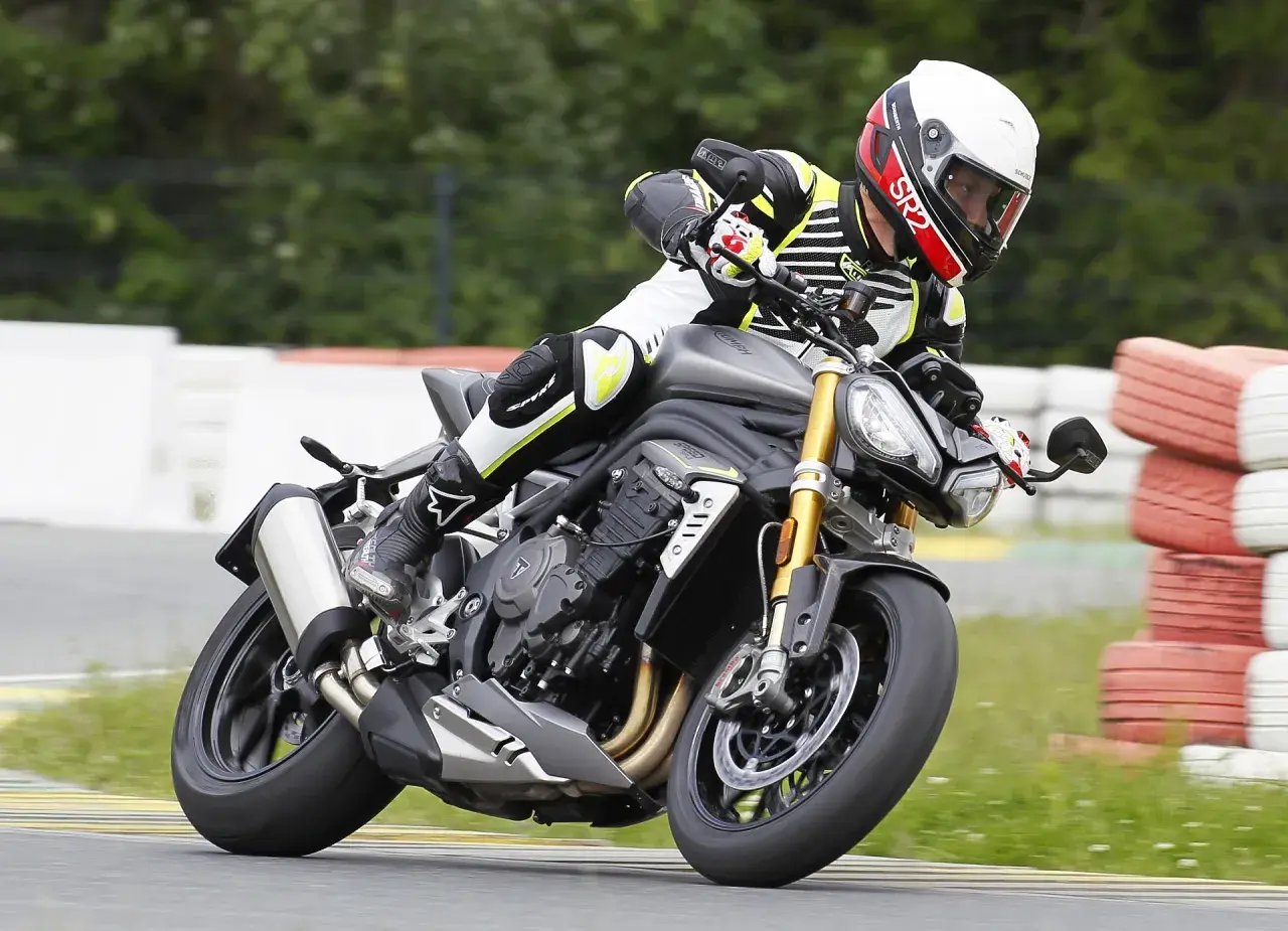 Motocyklista w kasku i kombinezonie pochyla się na torze wyścigowym na motocyklu Triumph Speed Triple.