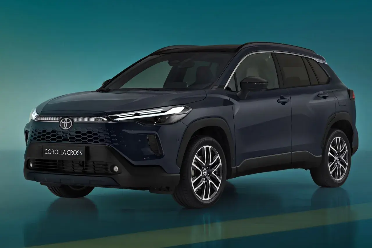 Nowa Toyota Corolla Cross w ciemnogranatowym kolorze, z nowoczesnym grillem i reflektorami LED, prezentuje się dynamicznie na tle turkusowego tła.