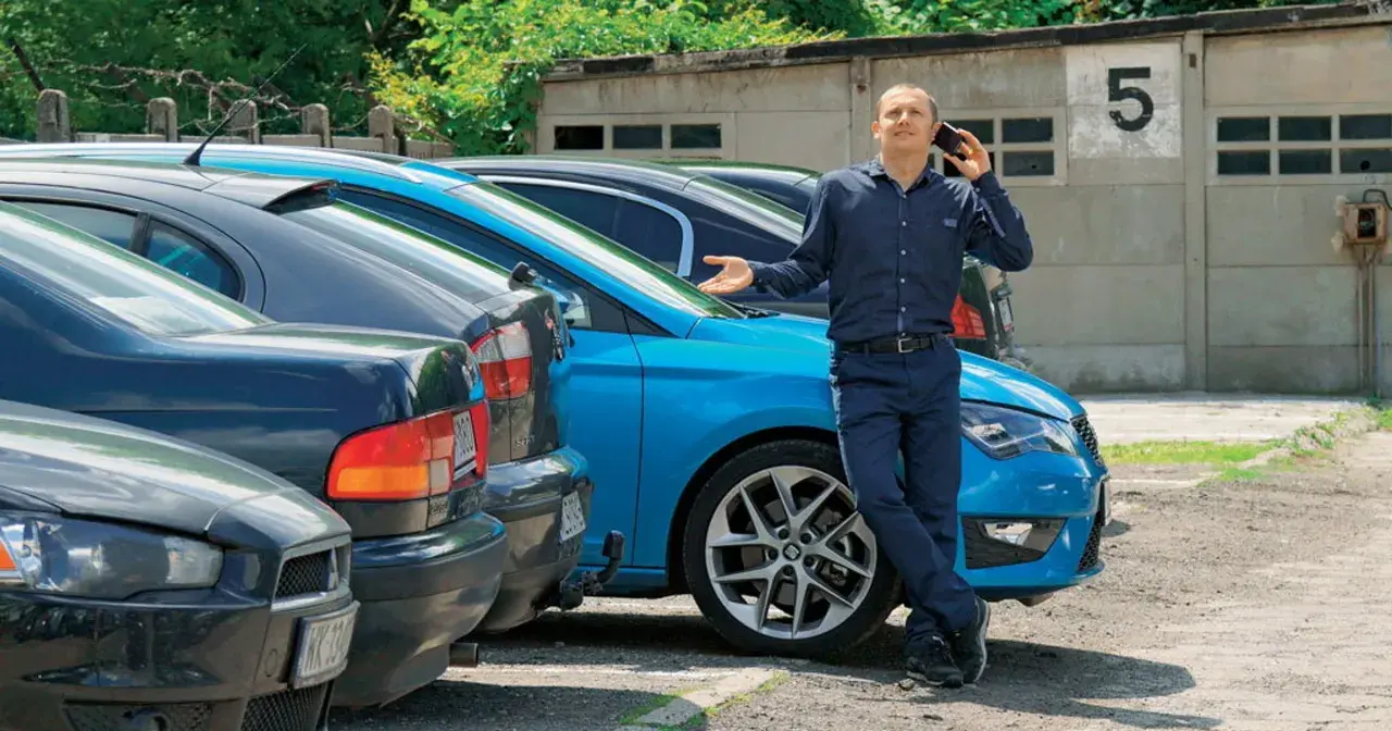 Mężczyzna rozmawia przez telefon, opierając się o niebieski samochód. Oferta: samochód bezpośrednio od właściciela.
