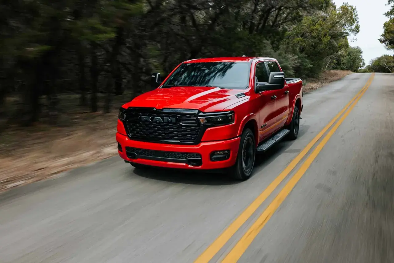 Czerwony Dodge Ram 1500 5.7 Hemi pędzi po krętej drodze wśród drzew.
