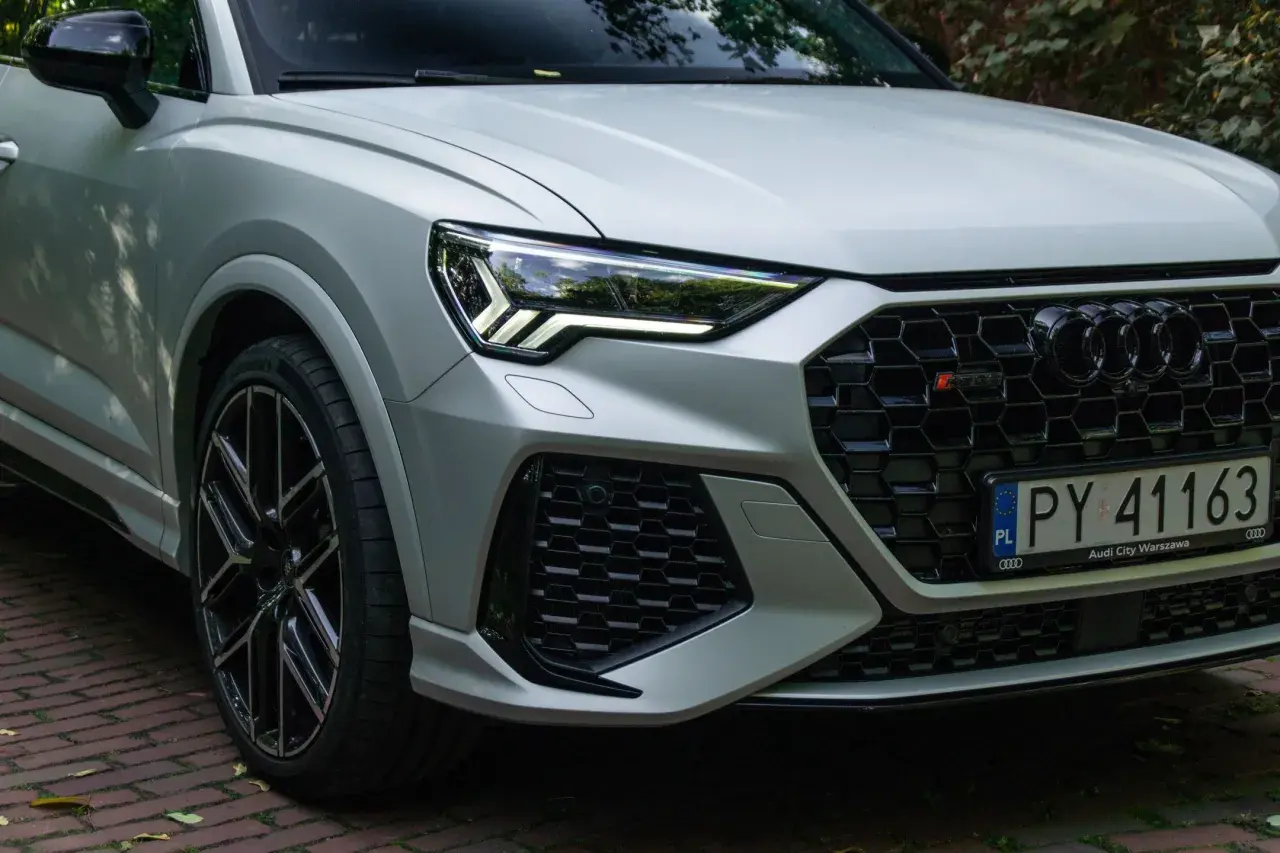 Srebrne Audi RS Q3 z czarnymi felgami i agresywnym grillem, gotowe do jazdy po warszawskich ulicach.