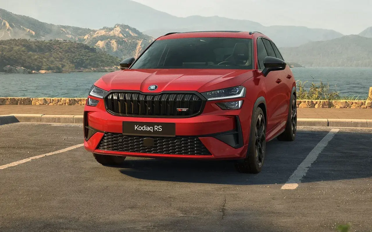 Czerwony Skoda Kodiaq RS zaparkowany nad jeziorem, z górami w tle.