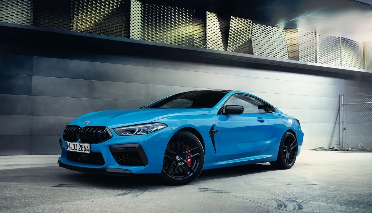 Niebieskie BMW M8 Coupe na tle nowoczesnej architektury.