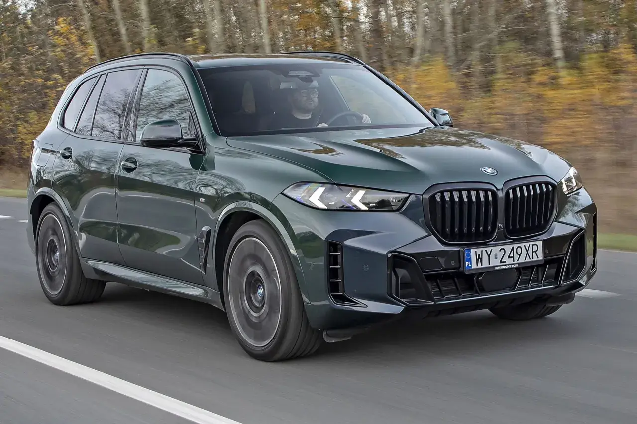 Zielony BMW X5 M50d pędzi po drodze, otoczony jesiennym lasem.