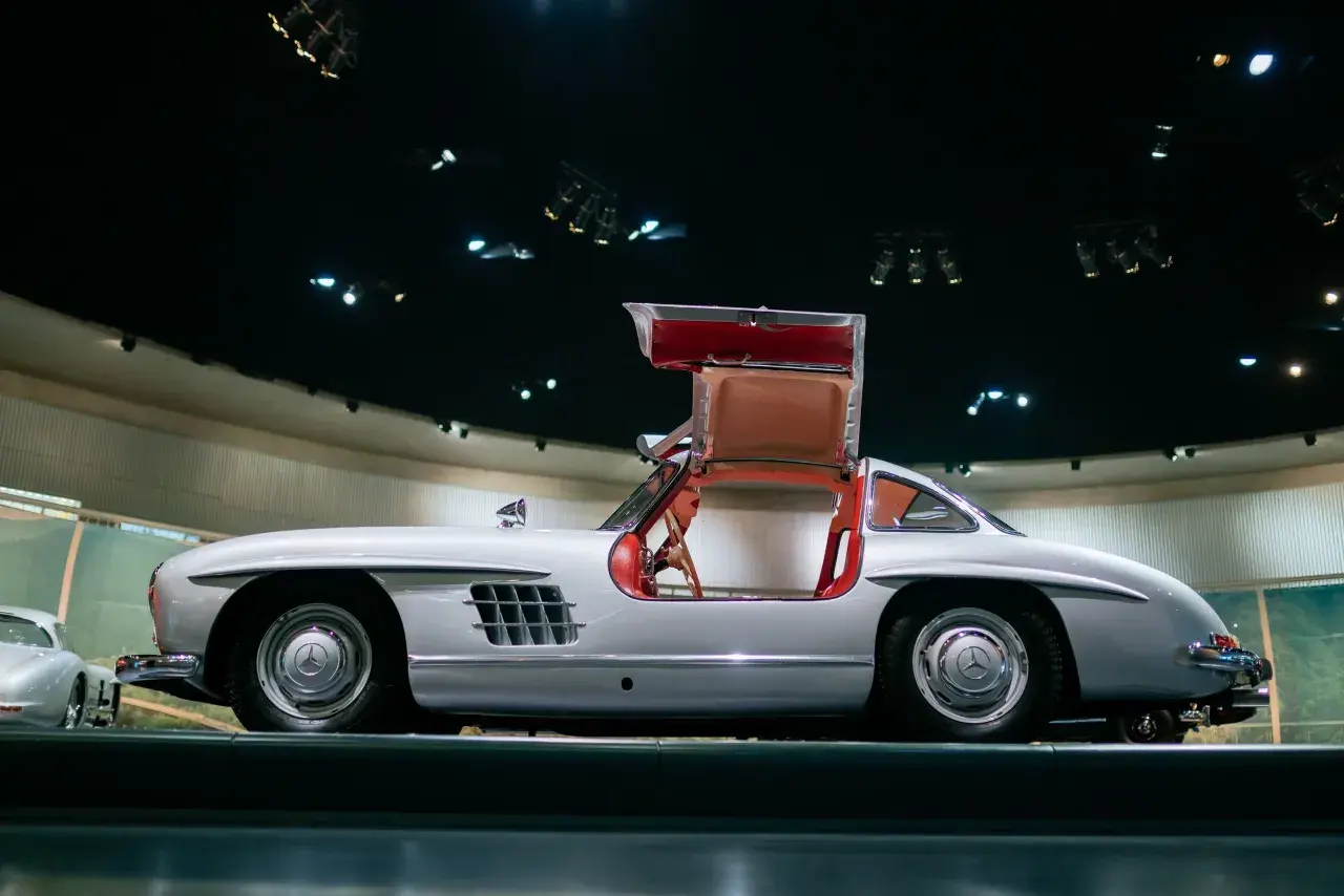 Srebrny Mercedes 300 SL z charakterystycznymi drzwiami otwieranymi do góry, prezentowany w muzeum.