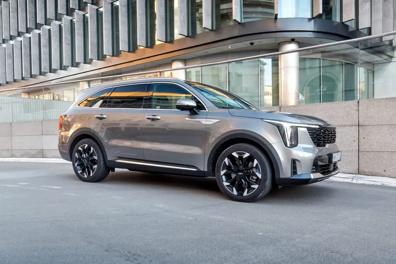 Elegancki, szary Kia Sorento 2025 z czarnymi felgami stoi przed nowoczesnym budynkiem.