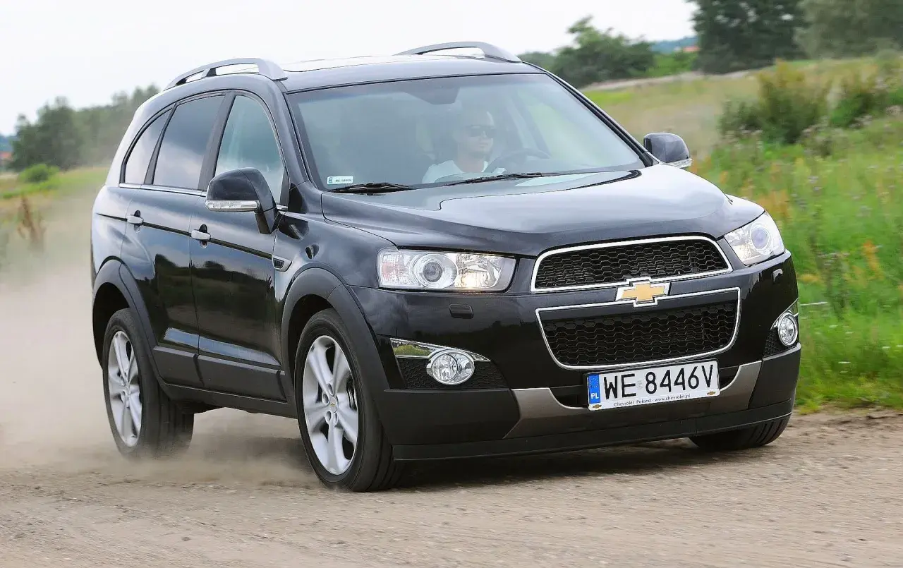 Czarny Chevrolet Captiva z kierowcą w okularach przeciwsłonecznych jedzie po piaszczystej drodze, wzbijając kurz.