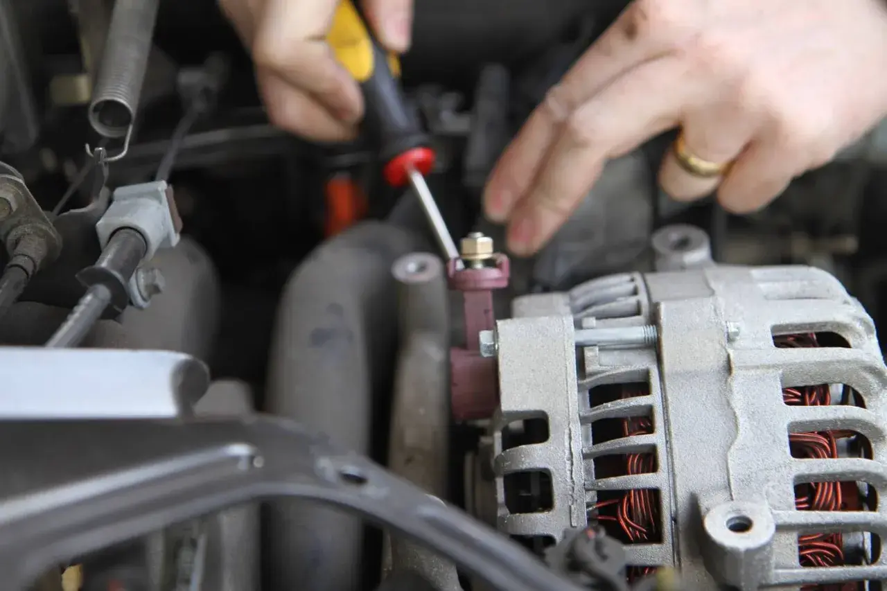 Dłonie mechanika odkręcają śrubę przy alternatorze samochodu.