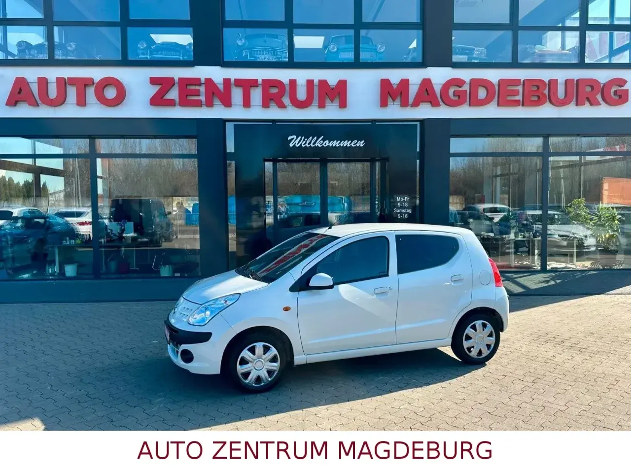 Biały Nissan Pixo zaparkowany przed salonem Auto Zentrum Magdeburg.