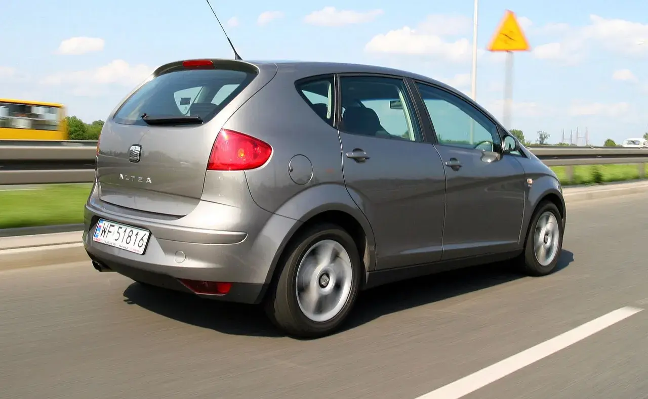 Szary Seat Altea XL jedzie po autostradzie. W tle widać żółty autobus i żółty znak ostrzegawczy.