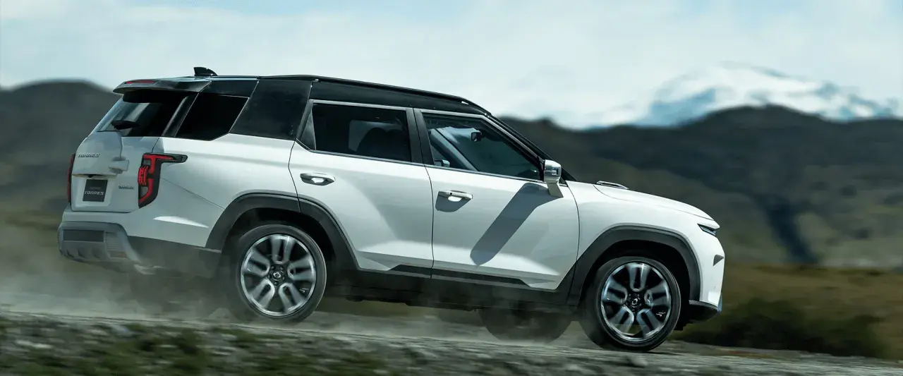 Biały SUV torres auto pokonuje wyboistą drogę, wzbijając tumany kurzu. W tle górzysty, surowy krajobraz.