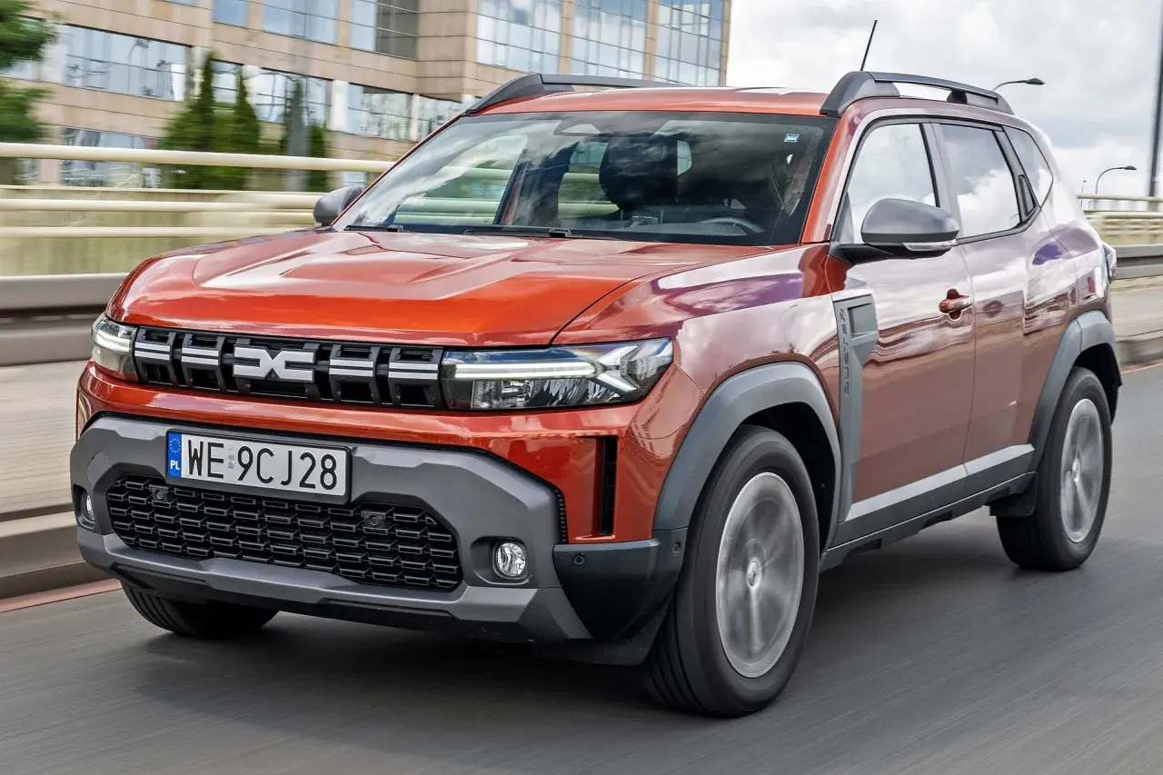 Pomarańczowy Renault Duster jedzie po drodze, z nowoczesnym designem i wyraźnym logo.