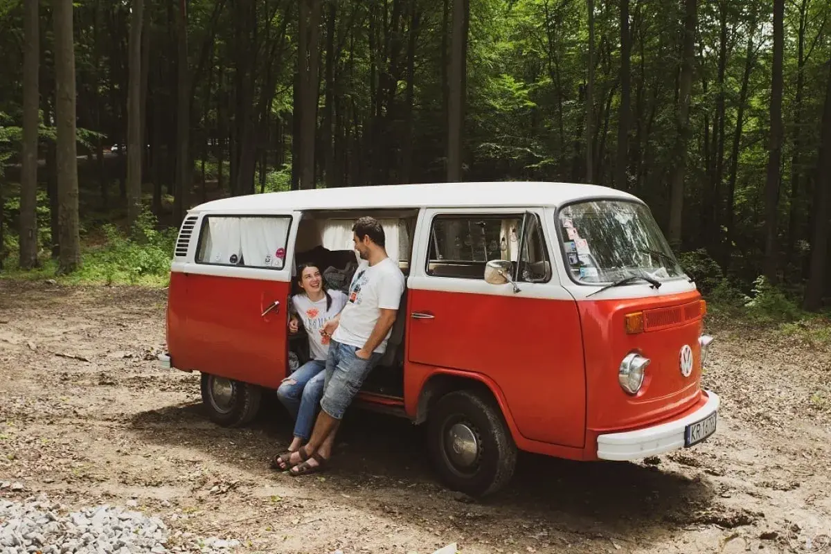 Para zakochanych odpoczywa przy swoim czerwono-białym vw t2 w lesie.