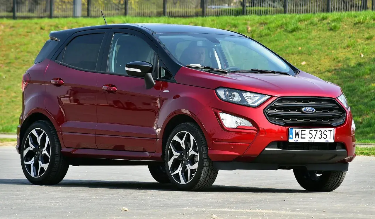 Czerwony Ford EcoSport z czarnym dachem, zaparkowany na tle zielonego zbocza.