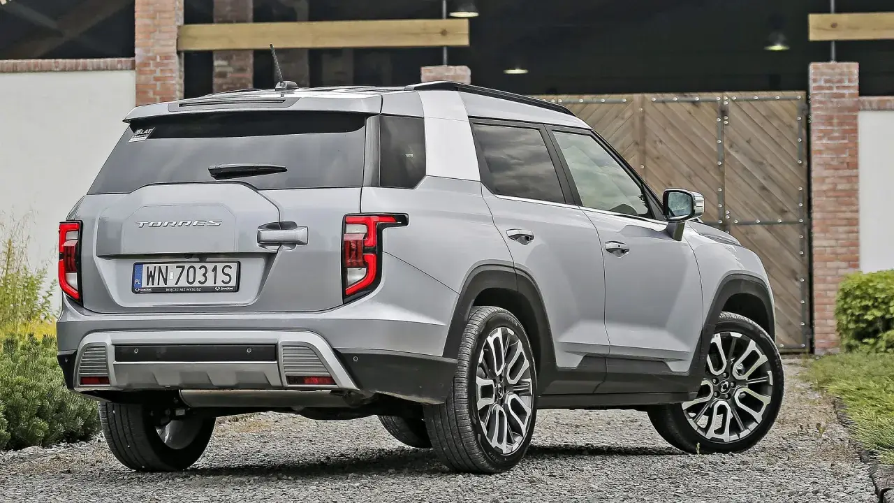 Srebrny SsangYong Torres z polskimi tablicami rejestracyjnymi WN 7031S stoi na żwirowej drodze przed drewnianą bramą.