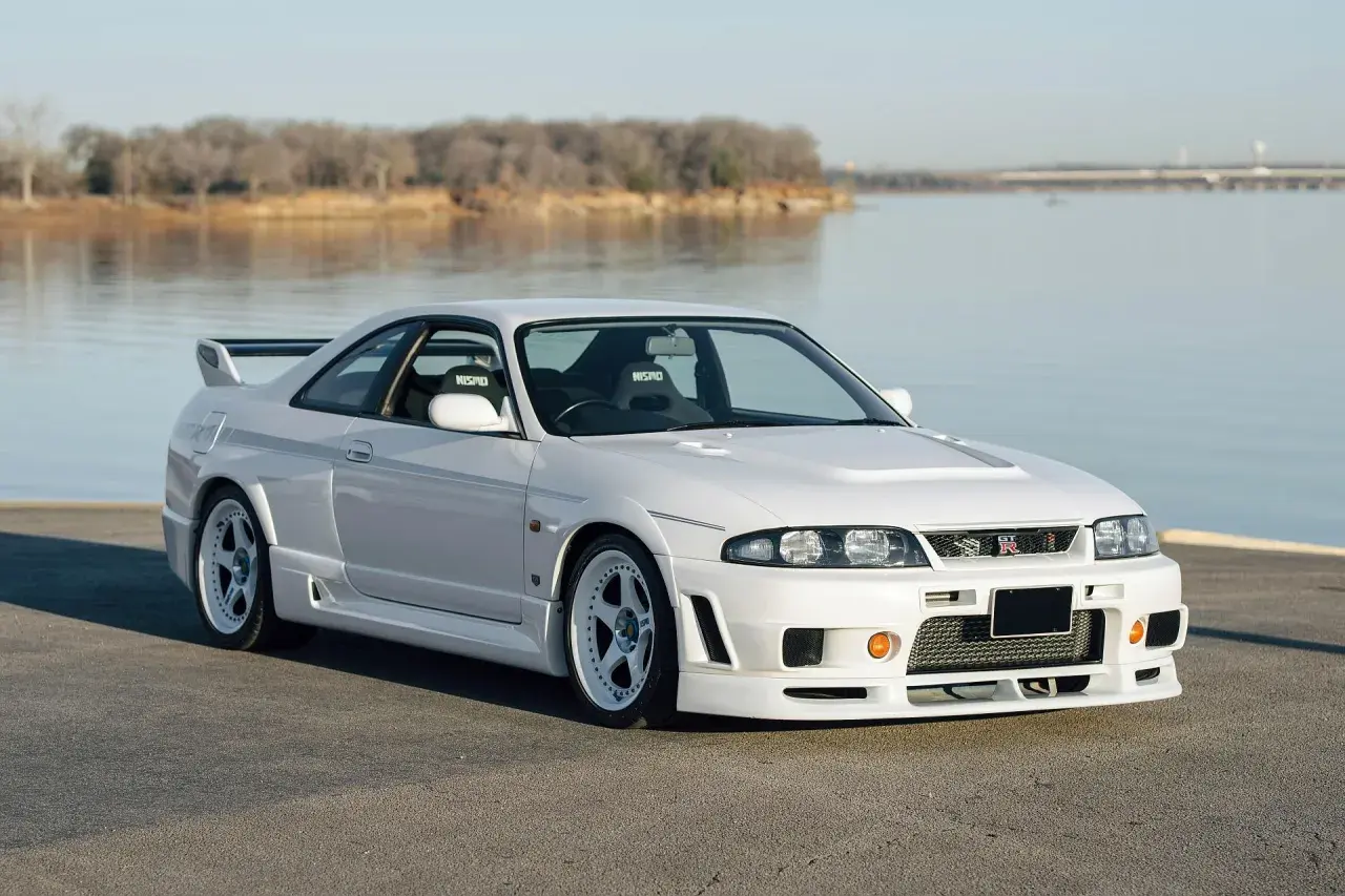 Białe r33 GT-R z siedzeniami Nismo stoi nad jeziorem.