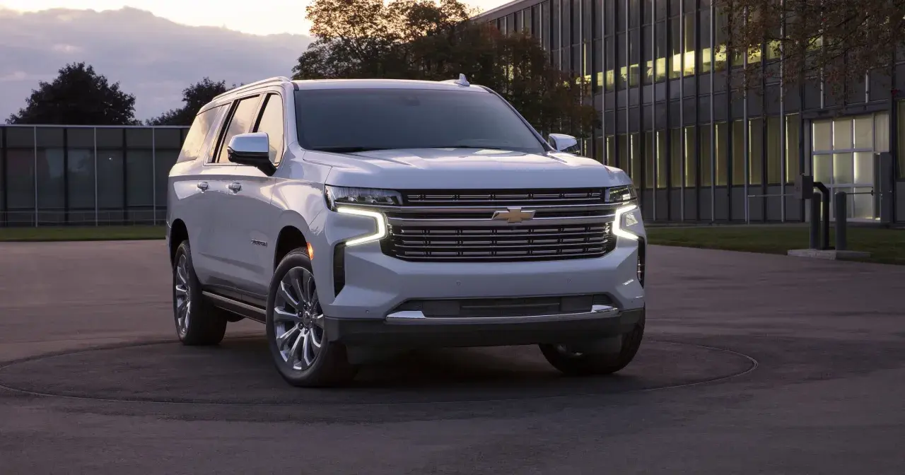 Biały Chevrolet Suburban zaparkowany przed nowoczesnym budynkiem.