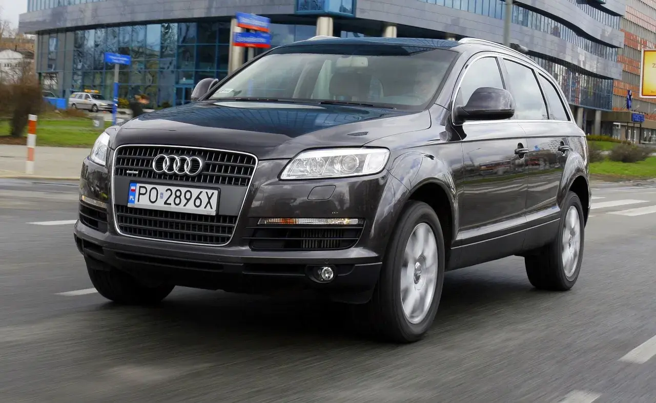 Ciemny Audi Q7 3.0 TDI w ruchu miejskim, z widocznym polskim numerem rejestracyjnym PO 2896X.