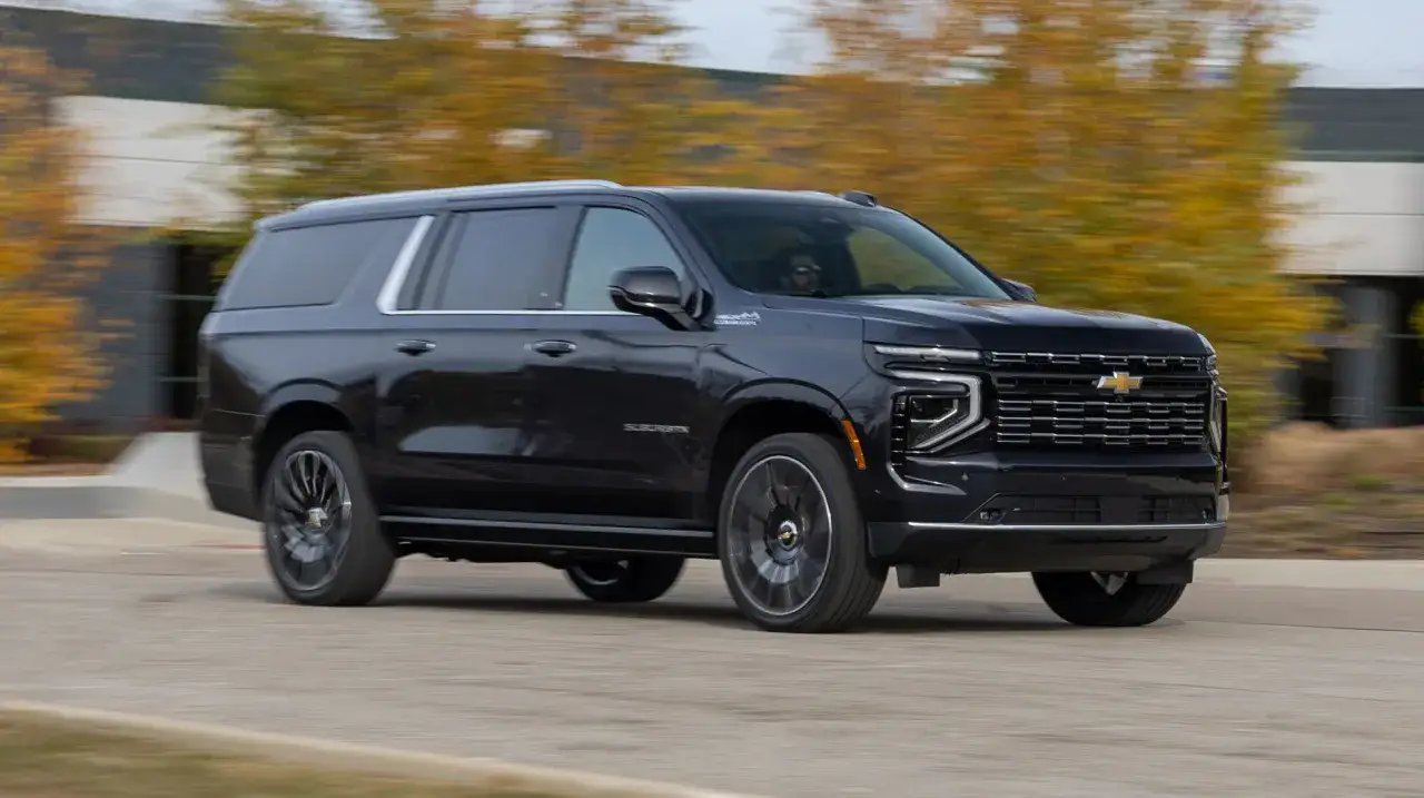 Czarny Chevrolet Suburban pędzi po drodze, otoczony jesiennymi drzewami.