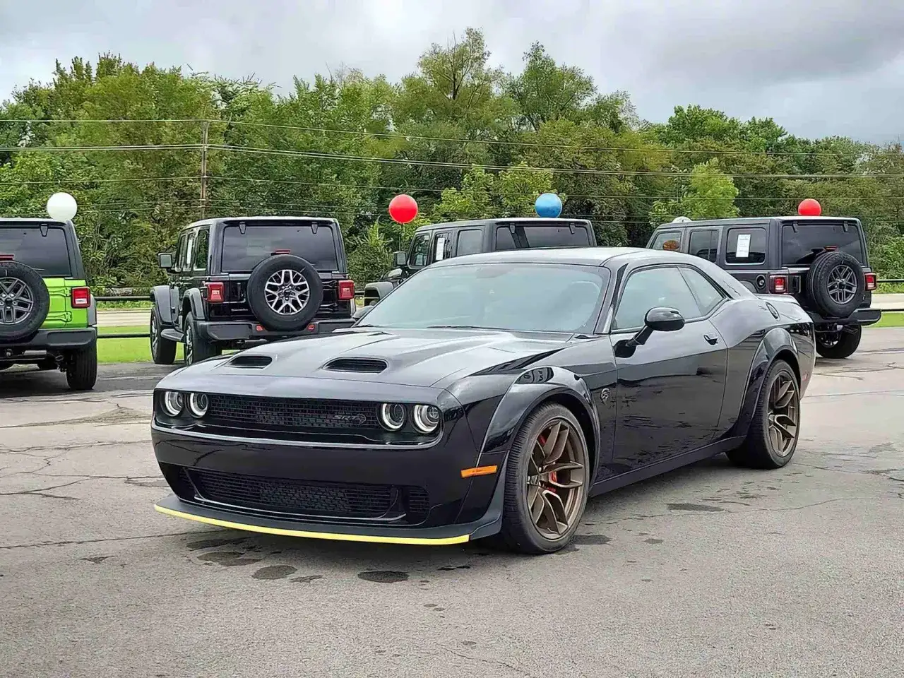 Czarny Dodge Challenger z żółtym akcentem na zderzaku, obok Jeepów. Sprawdź aktualną dodge challenger cena!