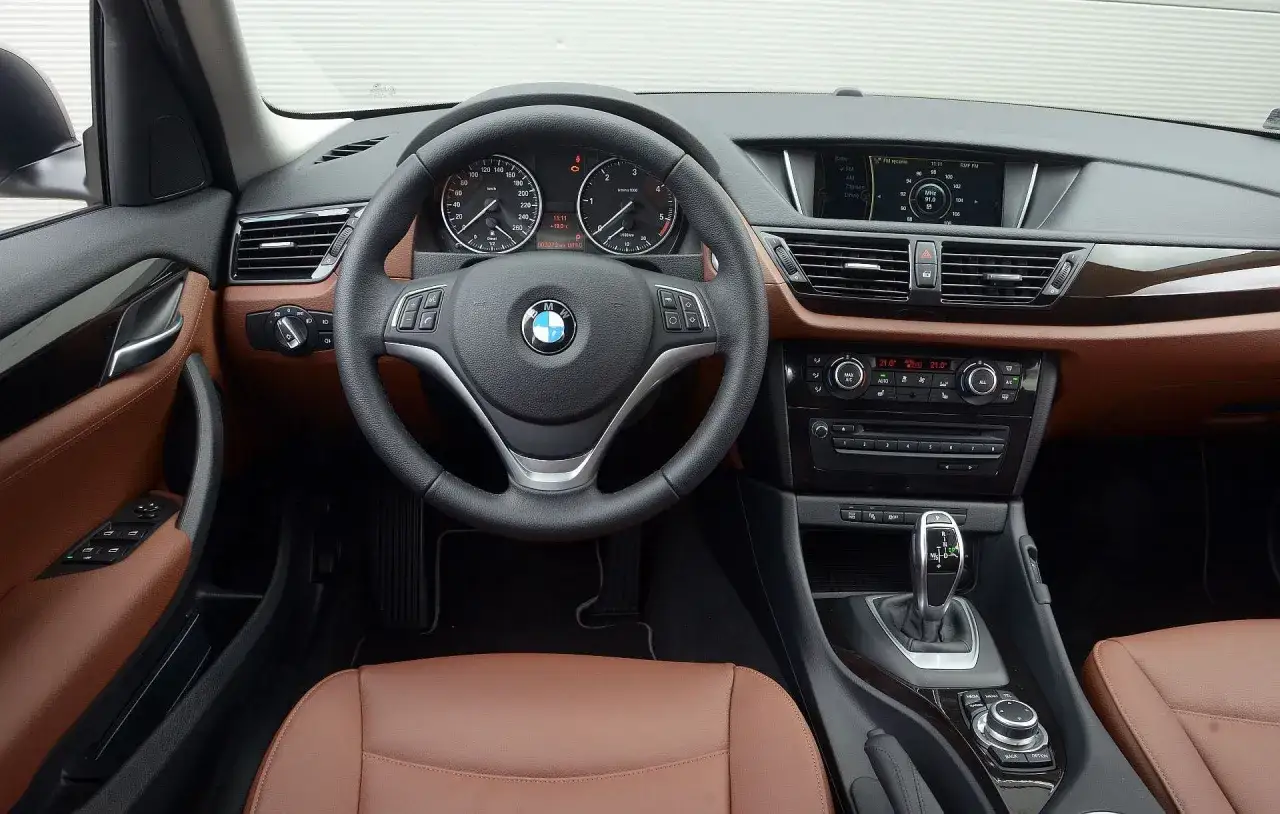 Wnętrze BMW X1 E84 z brązową skórzaną tapicerką, kierownicą i panelem środkowym.