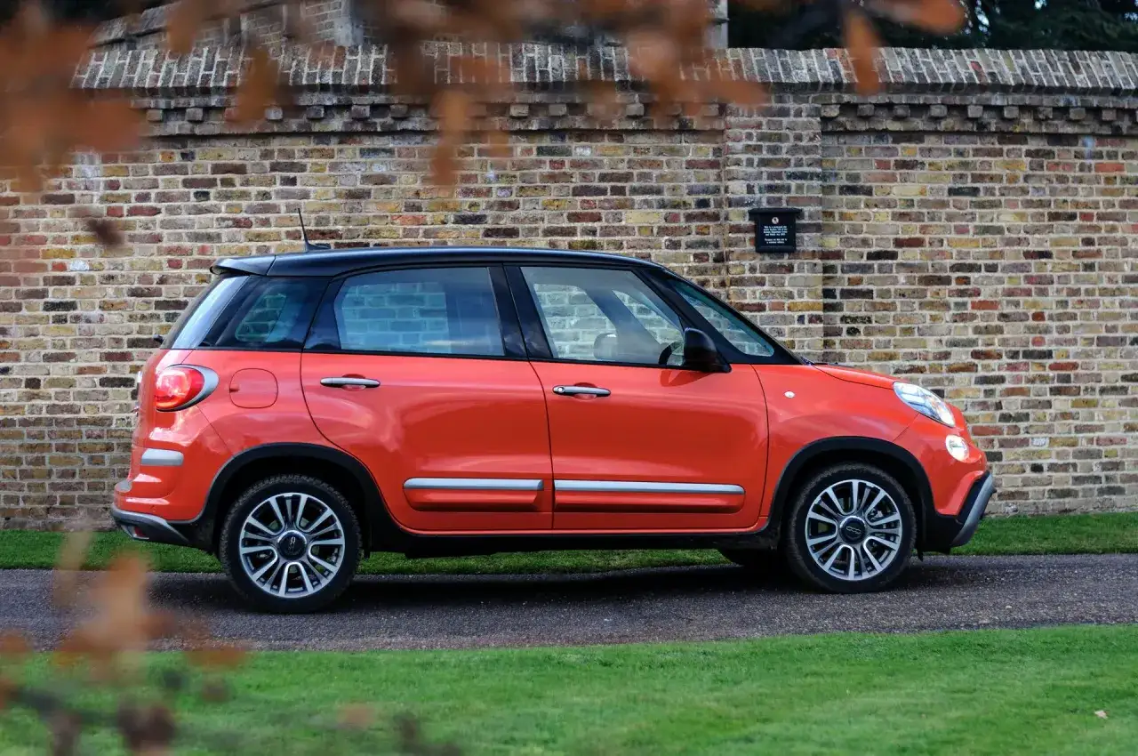Pomarańczowy Fiat 500 XL z czarnym dachem zaparkowany przy ceglanej ścianie.