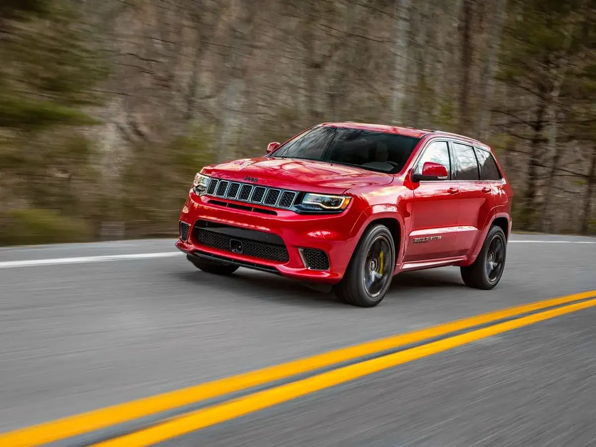 Czerwony Jeep Grand Cherokee Trackhawk pędzi po drodze, otoczony rozmytym lasem.