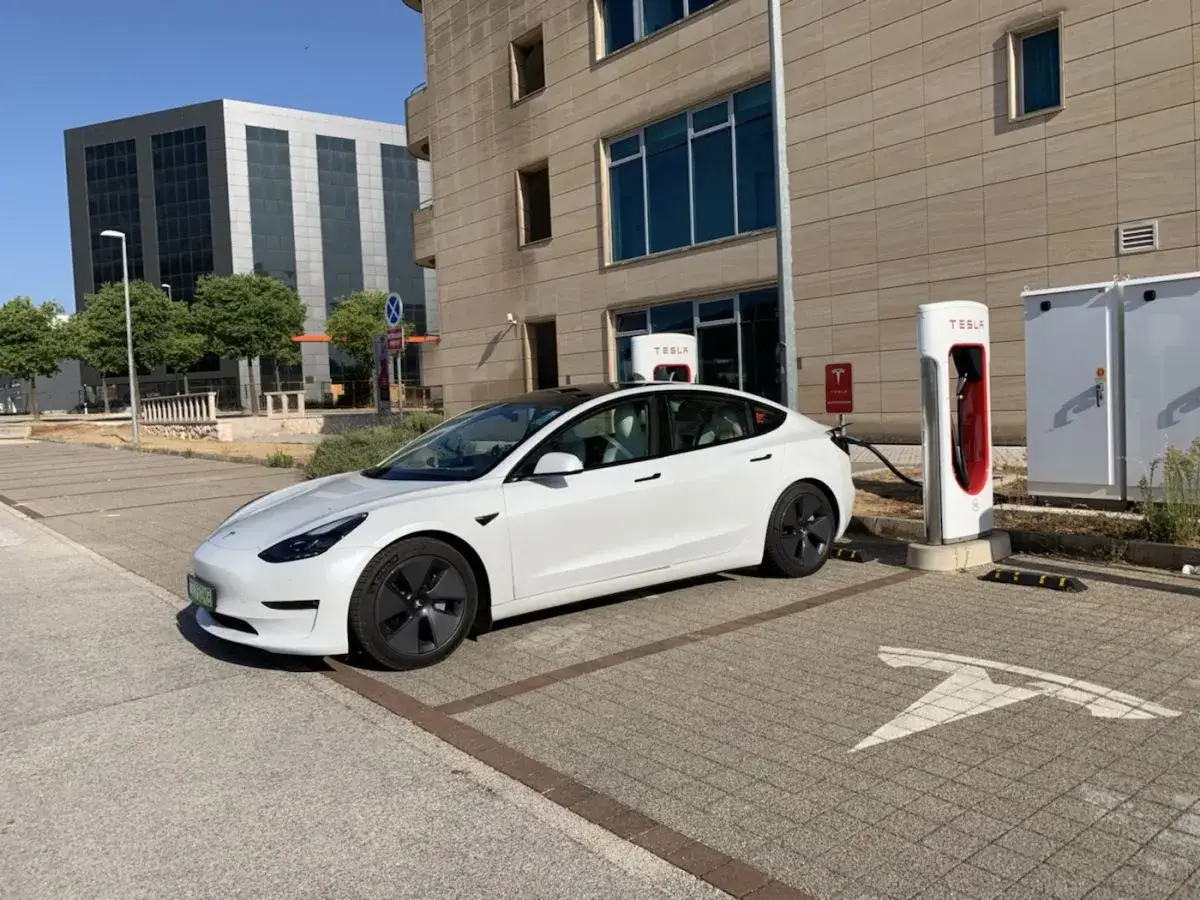 Biała Tesla Model 3 ładuje się przy stacji Supercharger. Potężny tesla moc silnika zapewnia ekologiczne podróżowanie.