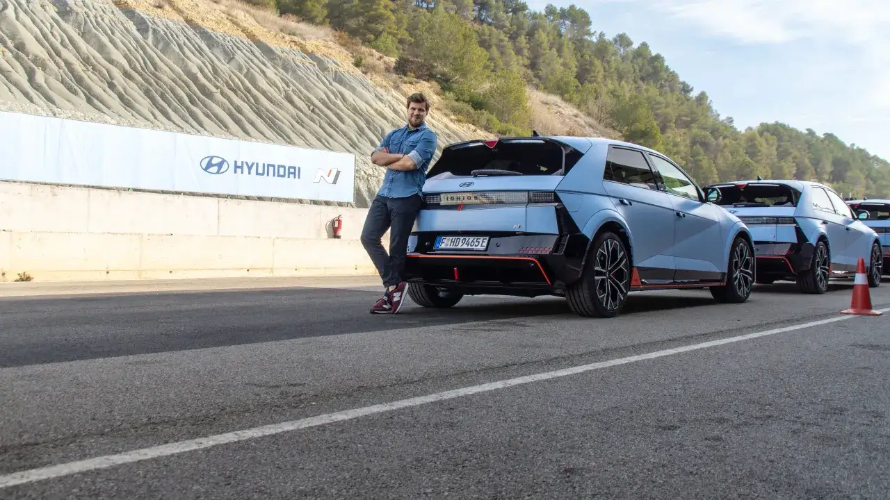 Mężczyzna opiera się o niebieskiego Hyundai Ioniq 5 N na torze wyścigowym. W tle baner Hyundai N.