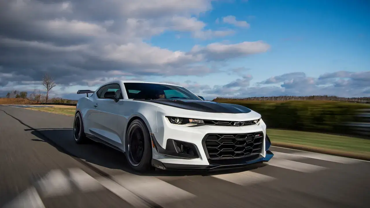 Białe Camaro ZL1 z czarną maską pędzi po torze wyścigowym, zostawiając za sobą rozmyte tło.