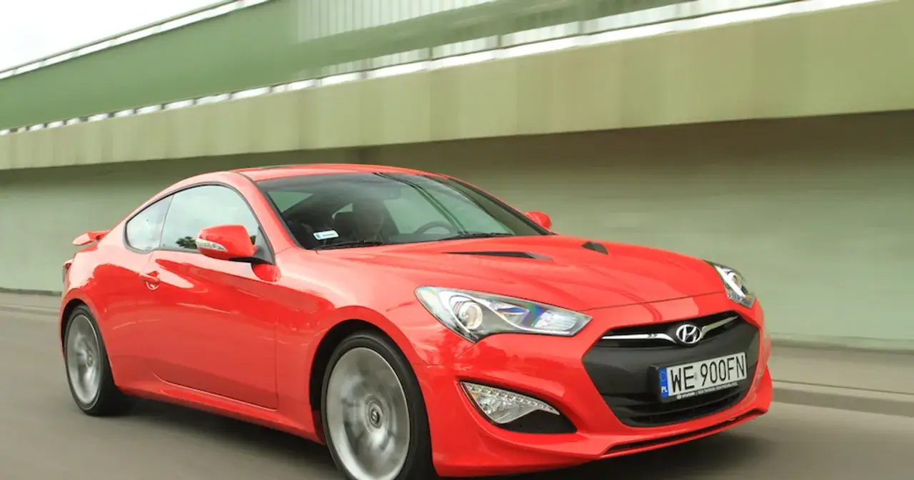 Czerwony Hyundai Genesis Coupe 3.8 V6 pędzi pod zielonym wiaduktem.