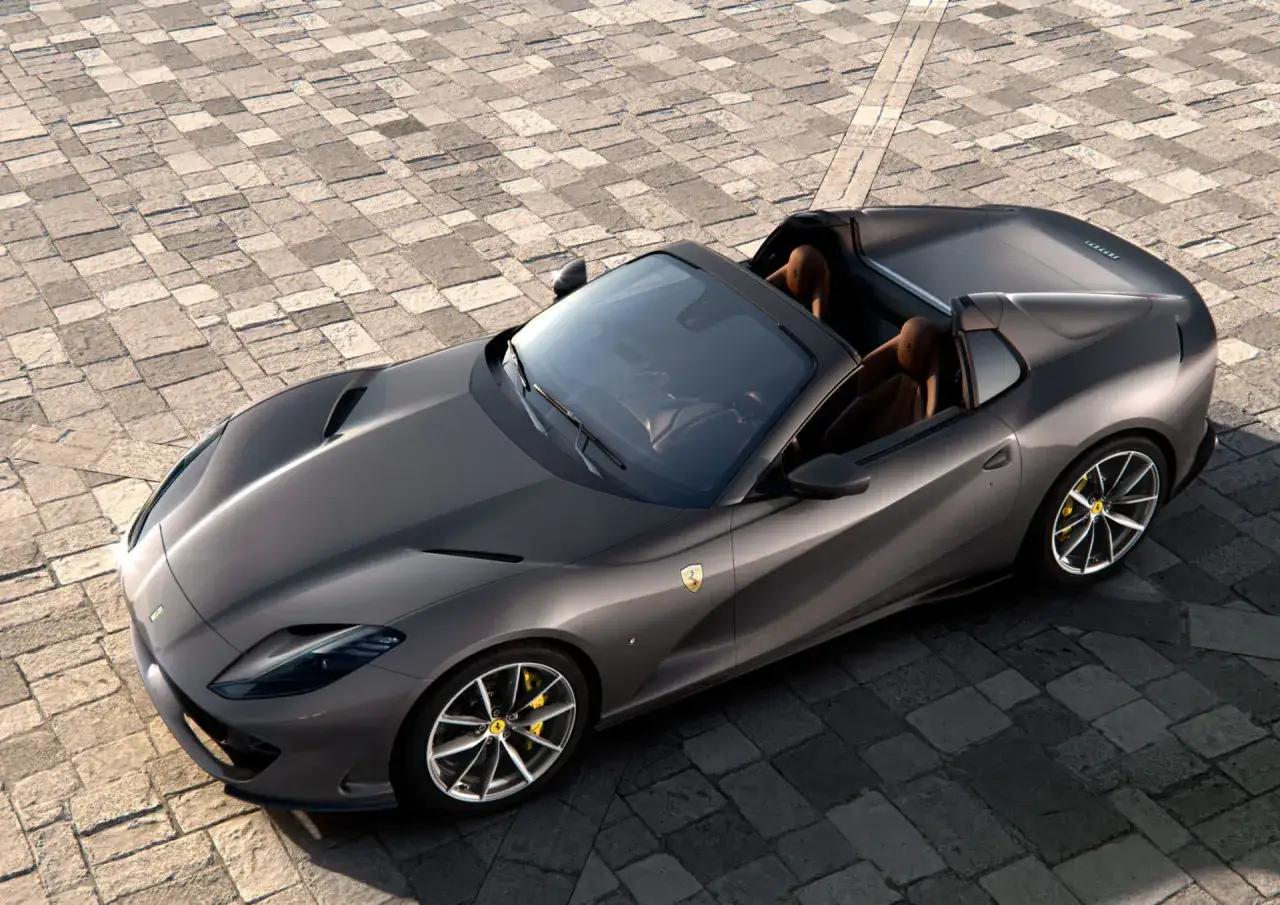 Szary kabriolet Ferrari 812 GTS z brązowym wnętrzem na brukowanej nawierzchni, gotowy do jazdy.