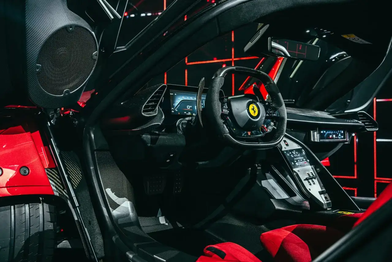 Wnętrze Ferrari F80: sportowa kierownica, cyfrowe zegary i czerwone fotele.
