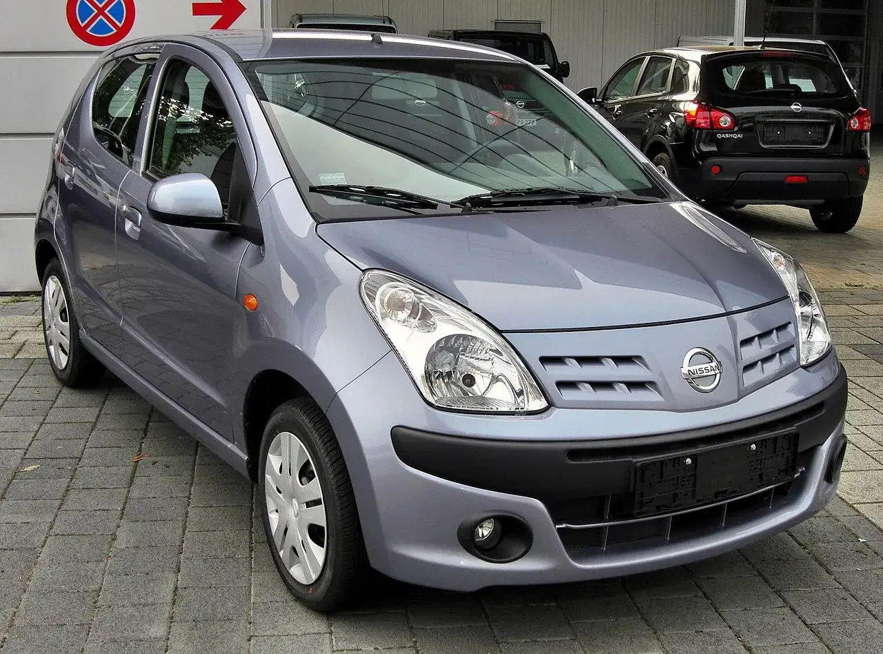 Szary Nissan Pixo stoi na chodniku. Obok widać czarnego Nissana Qashqai.