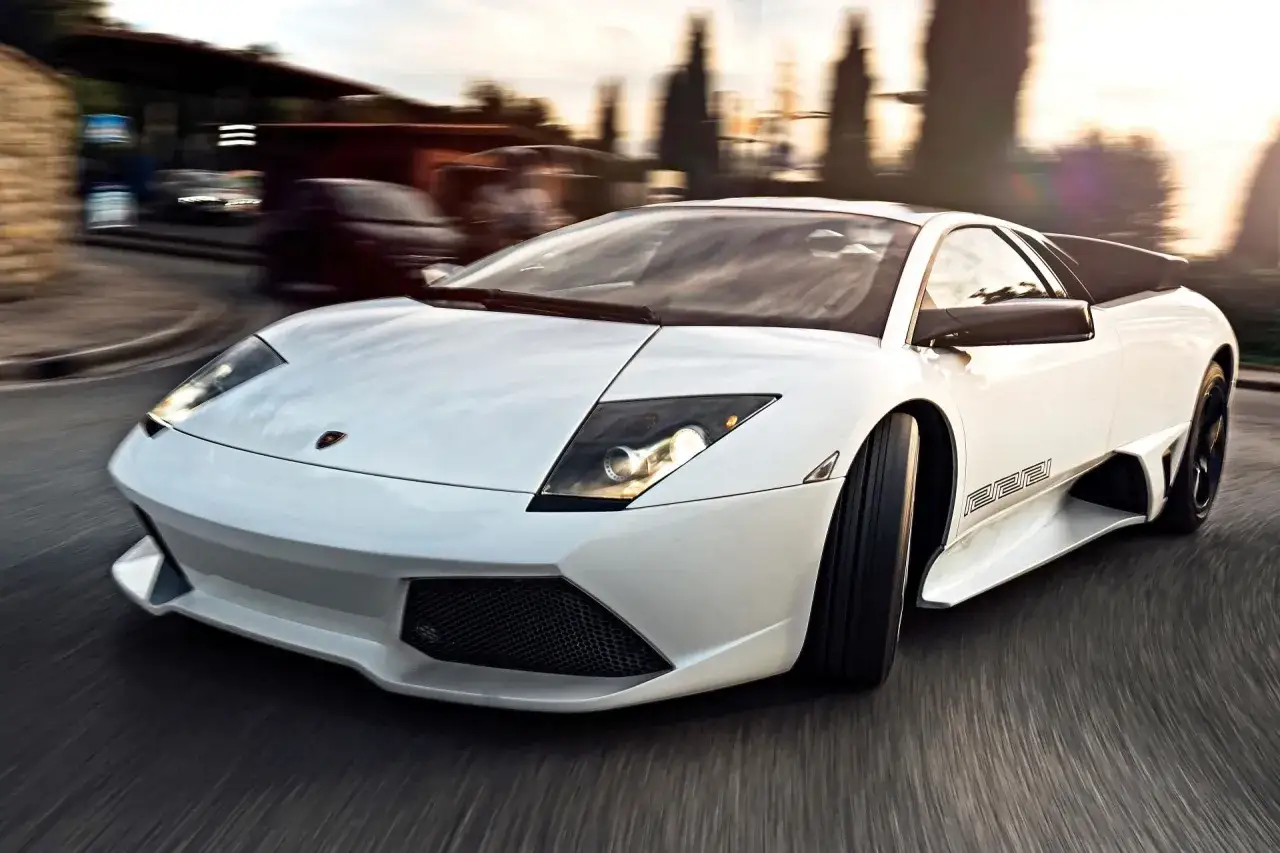Biały Lamborghini Murcielago pędzi po krętej drodze, rozmazując tło.