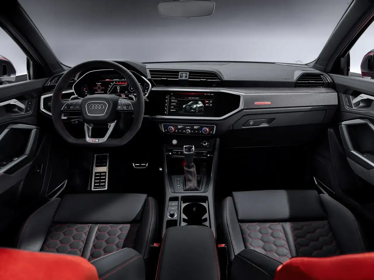 Wnętrze Audi RS Q3 z czarnymi skórzanymi fotelami i czerwonymi przeszyciami. Kierownica sportowa, cyfrowe zegary i ekran multimedialny.