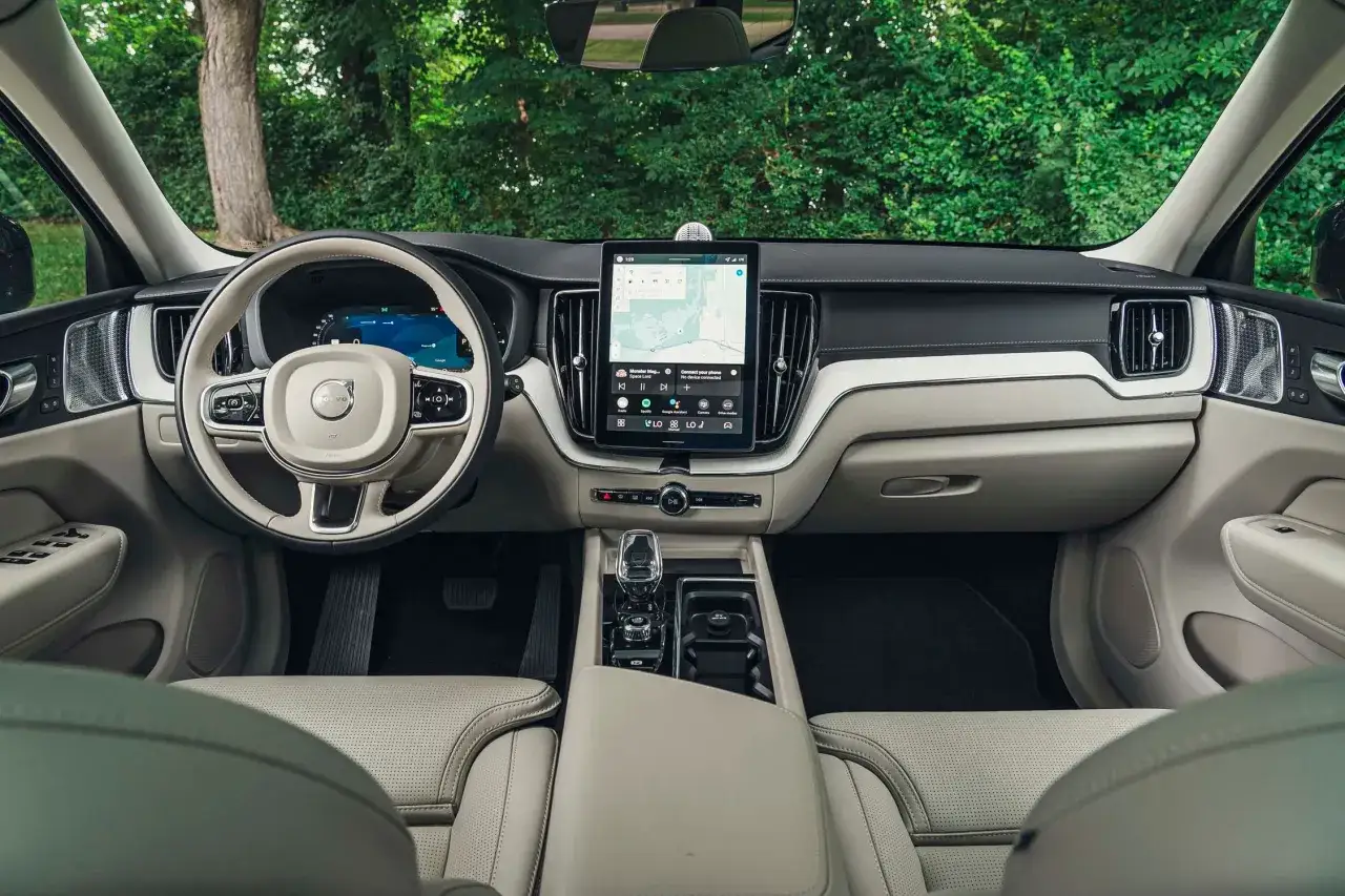Wnętrze Volvo XC60 2026 z dużym ekranem dotykowym, cyfrowymi zegarami i jasną, skórzaną tapicerką.