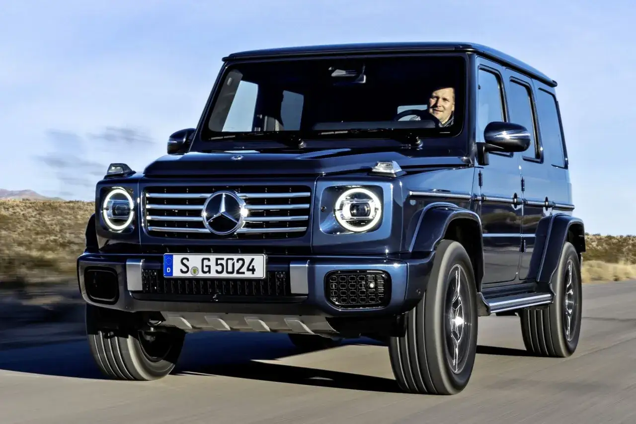 Ciemnoniebieski Mercedes G Klasa w ruchu. Kierowca uśmiecha się. Sprawdź aktualną mercedes g klasa cena.