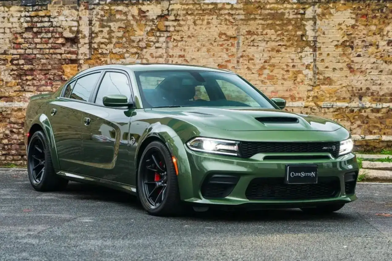 Zielony Dodge Charger SRT z czarnymi felgami i czerwonymi zaciskami hamulcowymi, zaparkowany przed ceglaną ścianą.