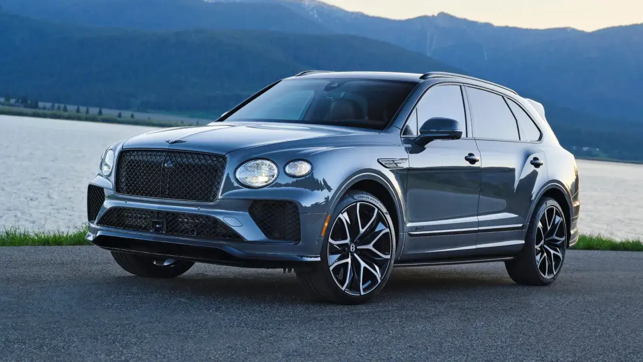 Szary Bentley SUV z imponującym grillem i felgami stoi nad jeziorem, w tle góry.