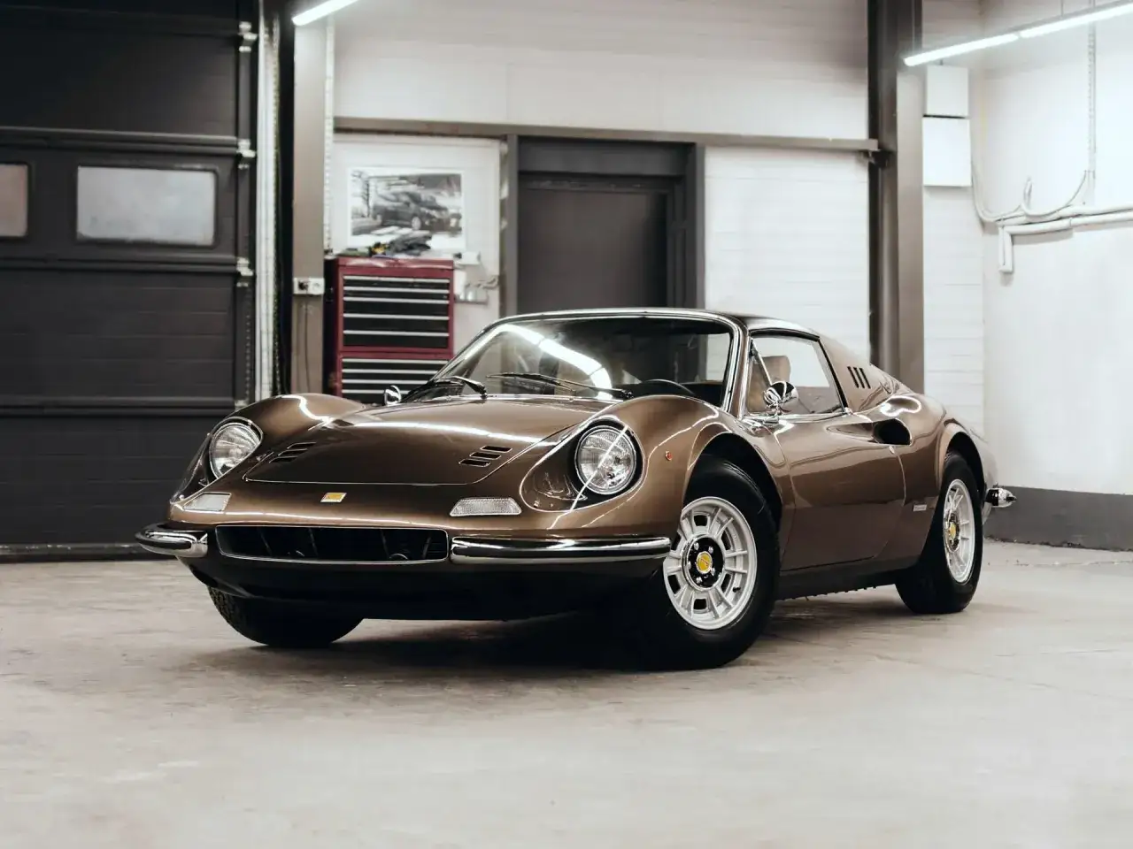 Brązowe Ferrari Dino 246 GT w garażu, z charakterystycznymi felgami i chromowanymi detalami.