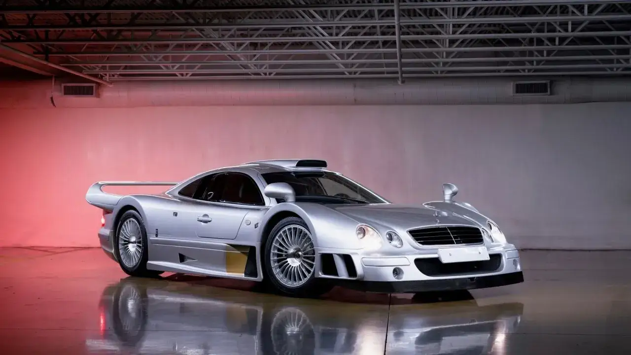 Srebrny Mercedes CLK GTR w garażu, z czerwonym światłem w tle. Ikona wyścigów.