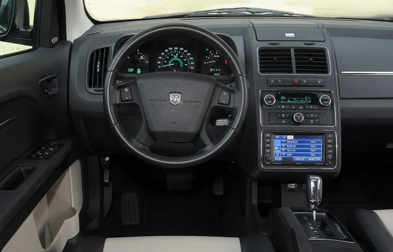 Wnętrze Dodge Journey 3.6: kierownica, deska rozdzielcza z ekranem multimedialnym i panelem klimatyzacji.