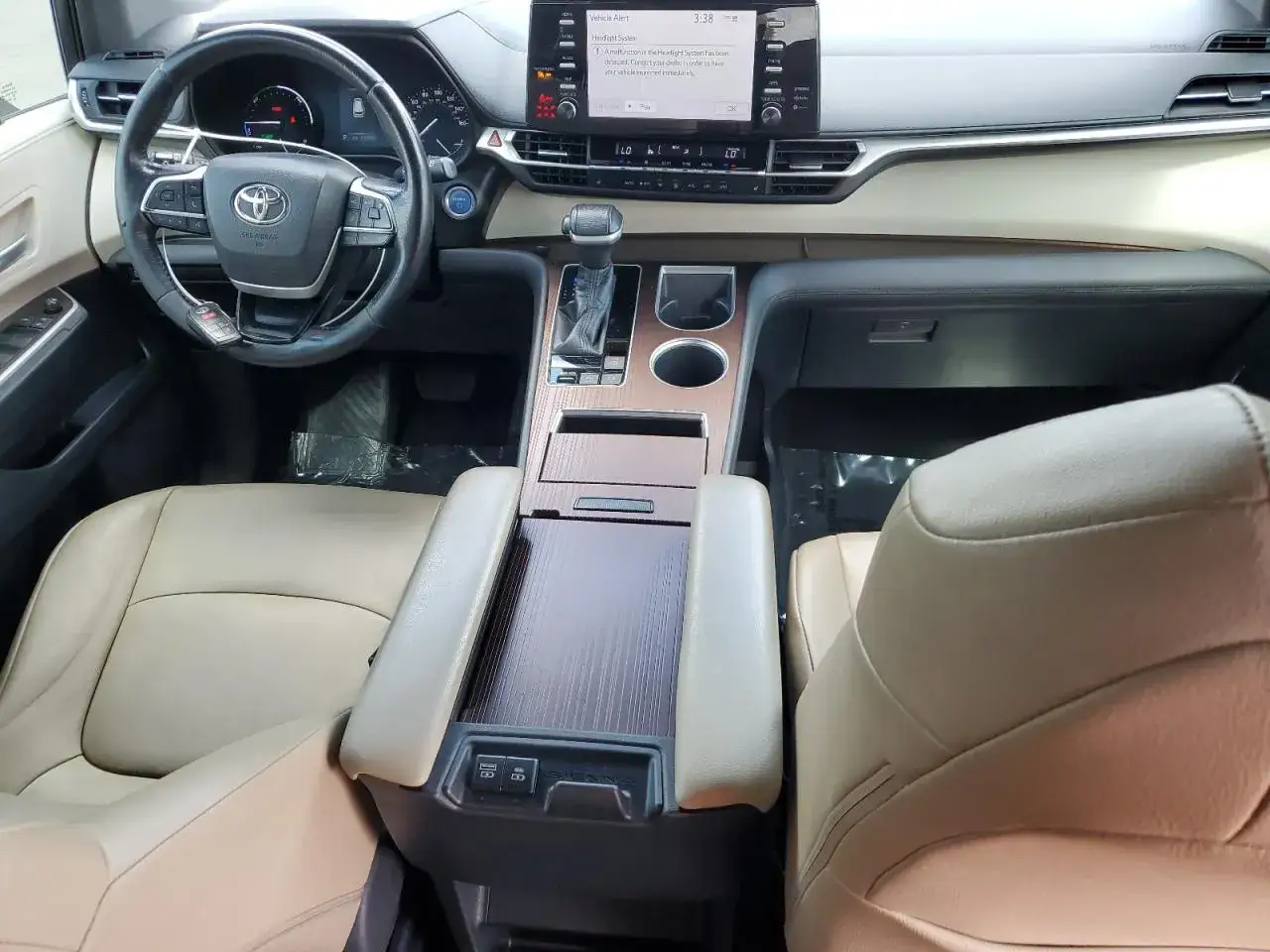 Wnętrze Toyoty Sienna w jasnej tapicerce, z drewnianymi akcentami i ekranem multimedialnym.