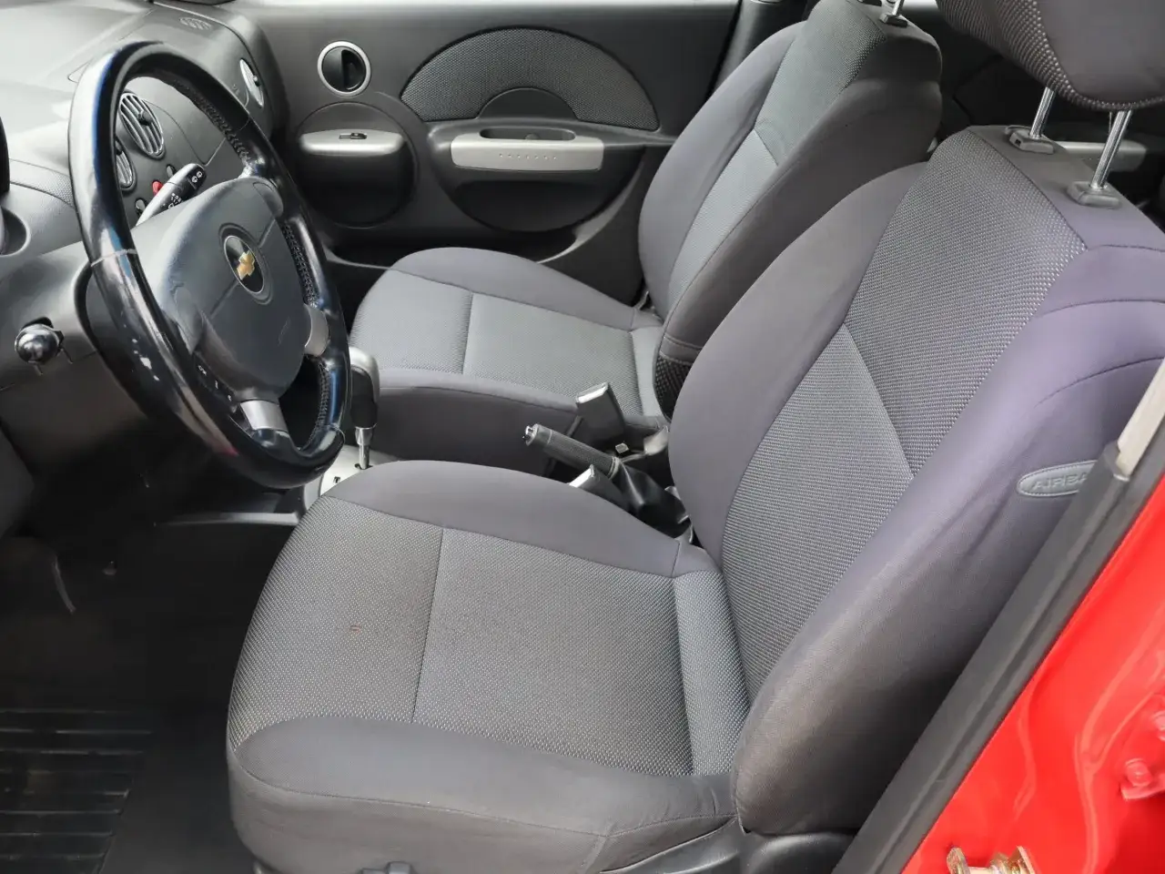 Wnętrze czerwonego Chevrolet Kalos: szare siedzenia, kierownica i deska rozdzielcza.