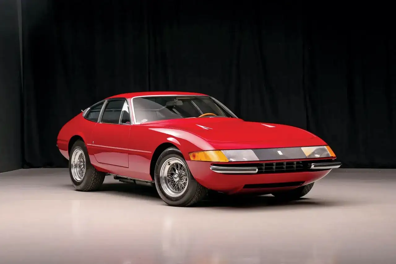 Klasyczny czerwony Ferrari Daytona, ikona motoryzacji, prezentuje swoje eleganckie linie na tle czarnej kurtyny.