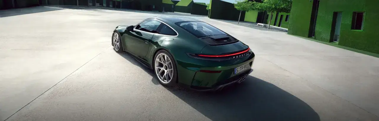 Zielony Porsche GT3 stoi na betonowym placu przed nowoczesnymi budynkami pokrytymi sztuczną trawą.