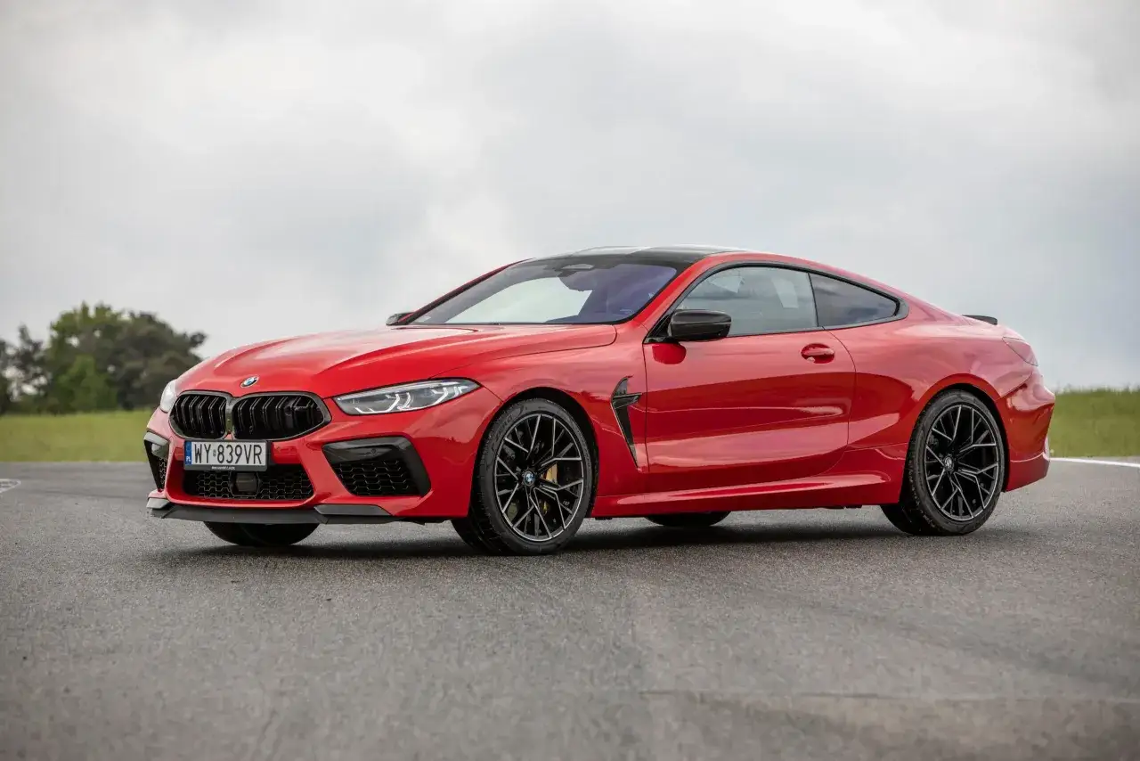 Czerwone BMW 840i z czarnym dachem i felgami, zaparkowane na torze wyścigowym.