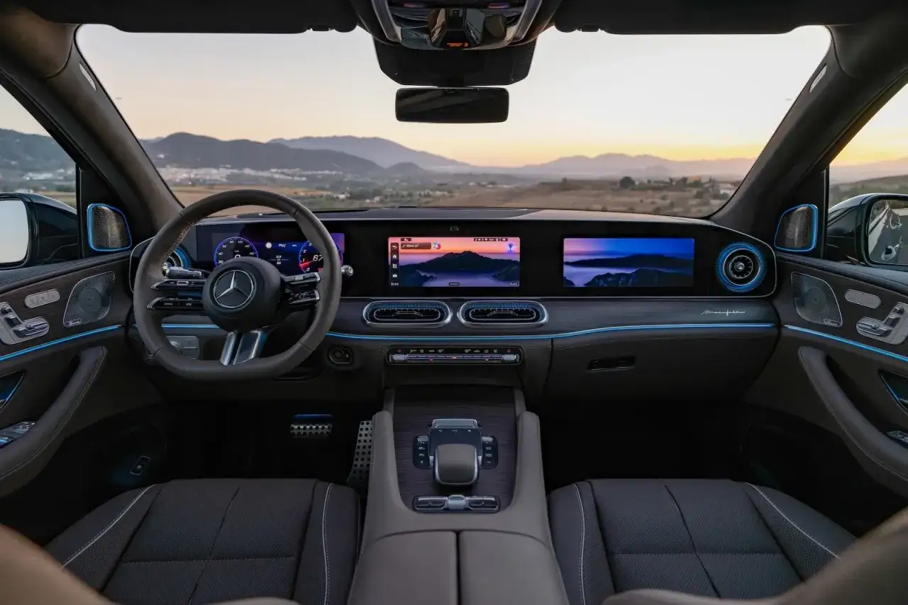 Wnętrze luksusowego Mercedes-Benz GLS z podświetleniem ambientowym i dwoma ekranami. Widok na górzysty krajobraz o zachodzie słońca.