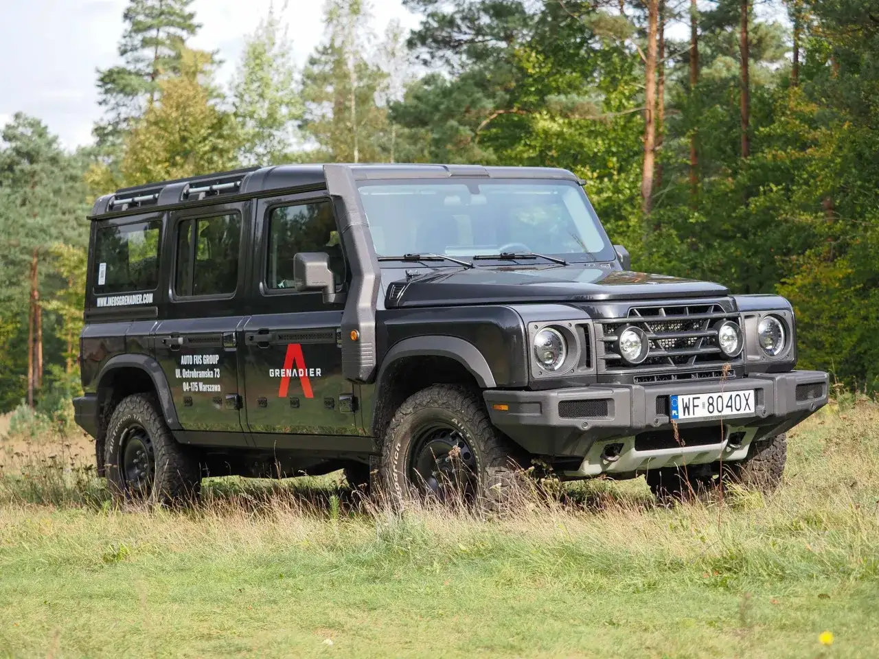 Czarny INEOS Grenadier stoi na trawiastym polu, gotowy na przygodę.